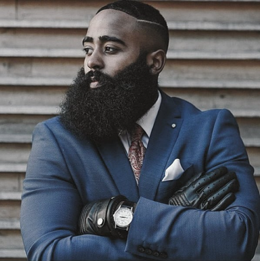 Man in a blue suit with a beard standing against a wooden background