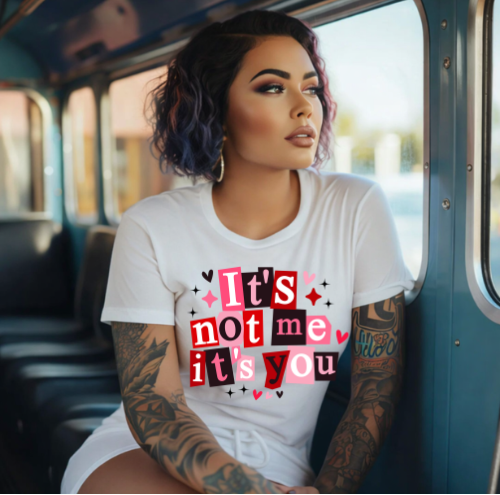 Woman sitting inside a vehicle wearing a white t-shirt with a colorful text design.