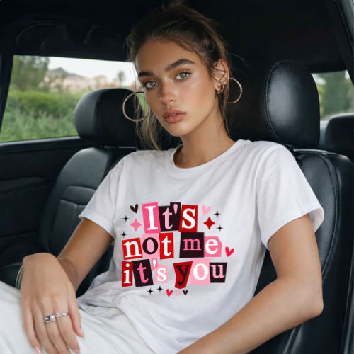 Woman sitting in a car wearing a white t-shirt with colorful text.