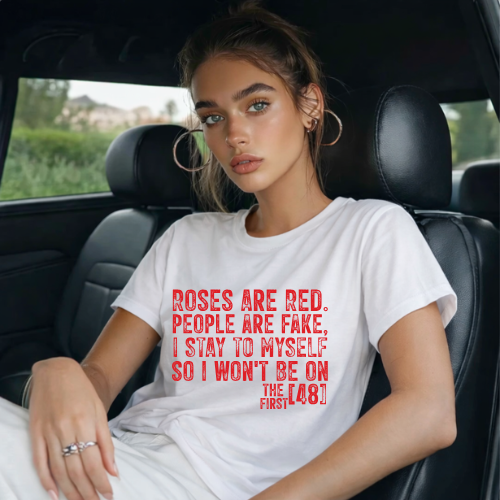 Woman sitting in a car wearing a white t-shirt with red text.